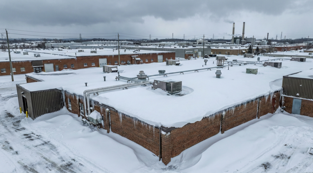 Commercial flat roof in Toronto buried under heavy snow drifts covering the parapet wall, illustrating the risk of structural stress from record snowfall.